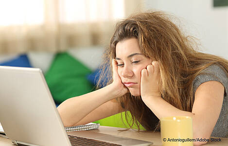 Eine junge Frau sitzt müde vor ihrem Laptop. Foto: Antonioguillem/Adobe Stock.