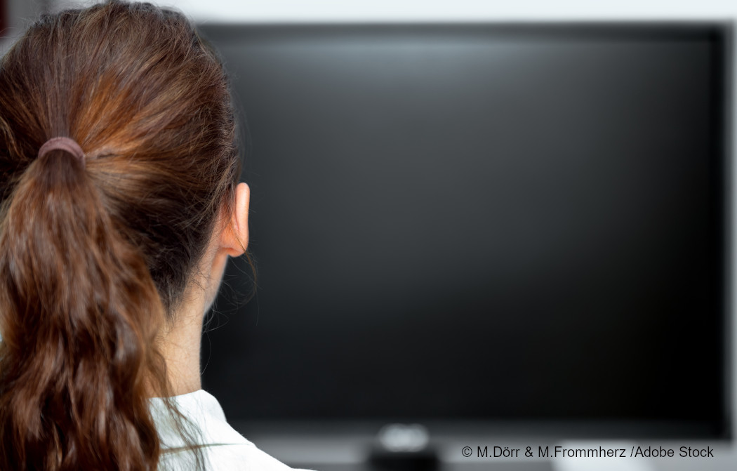Man sieht eine Frau von hinten vor einem schwarzen Bildschirm. Foto: M.Dörr & M.Frommherz/Adobe Stock.