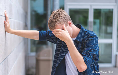 Verzweifelter Junge lehnt an einer Mauer und hat sein Gesicht in seiner Hand vergraben. Foto: Brian/Adobe Stock.