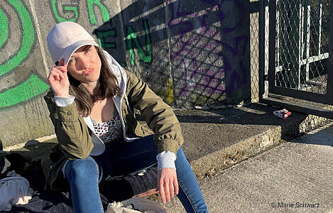 Marie Schwarz sitzt mit Basecap vor einer Mauer in der Sonne. Foto: Marie Schwarz.