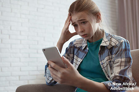 Hate Speech im Netz: Ein schockiertes Mädchen starrt auf sein Smartphone. Foto: New Africa/AdobeStock