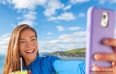 Ein Mädchen mit einem Getränk in der Hand macht mit dem handy ein Selfie. Foto: Maridav/Adobe Stock.