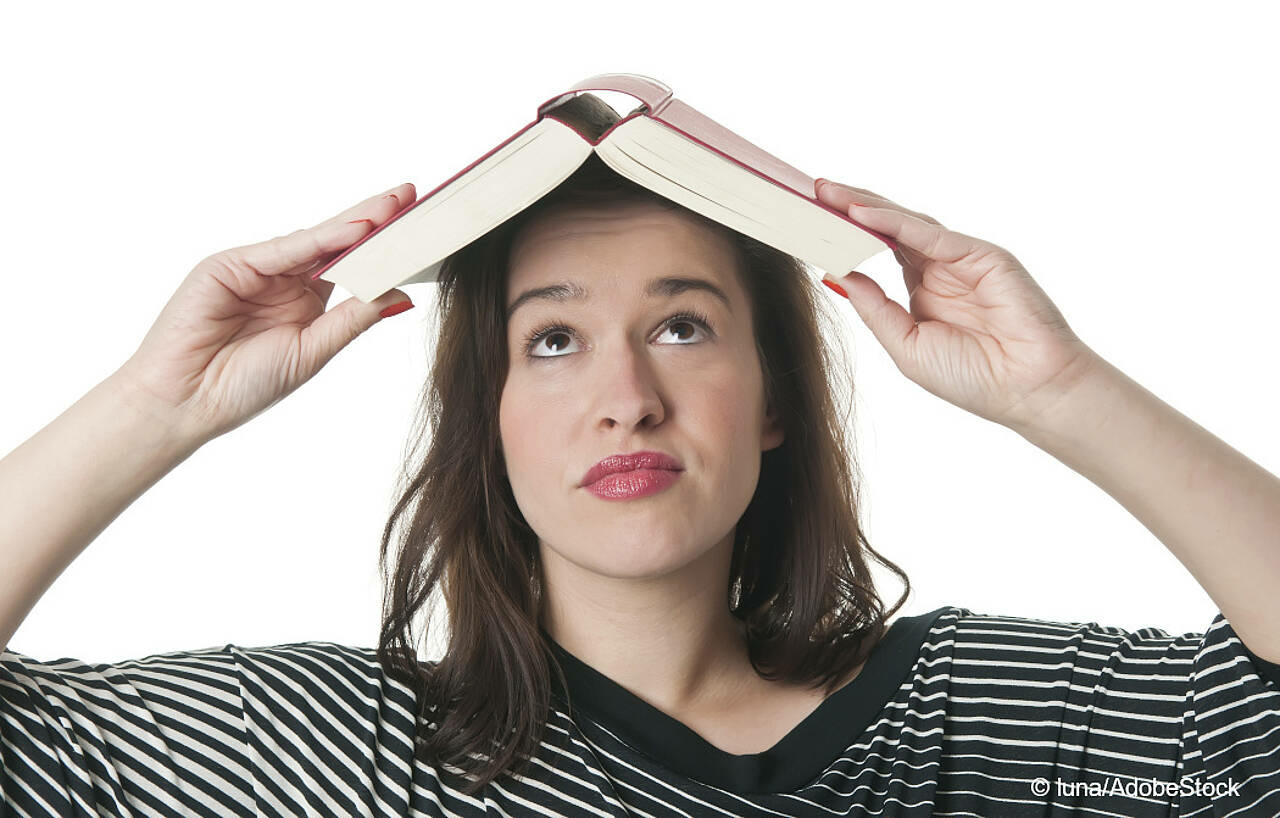 Eine junge Frau hält sich ein Buch über den Kopf. Foto: Luna/AdobeStock