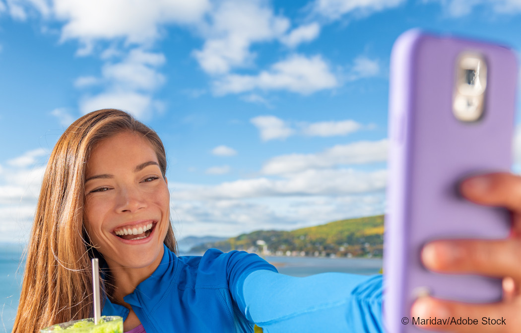 Ein Mädchen mit einem Getränk in der Hand macht mit dem handy ein Selfie. Foto: Maridav/Adobe Stock.